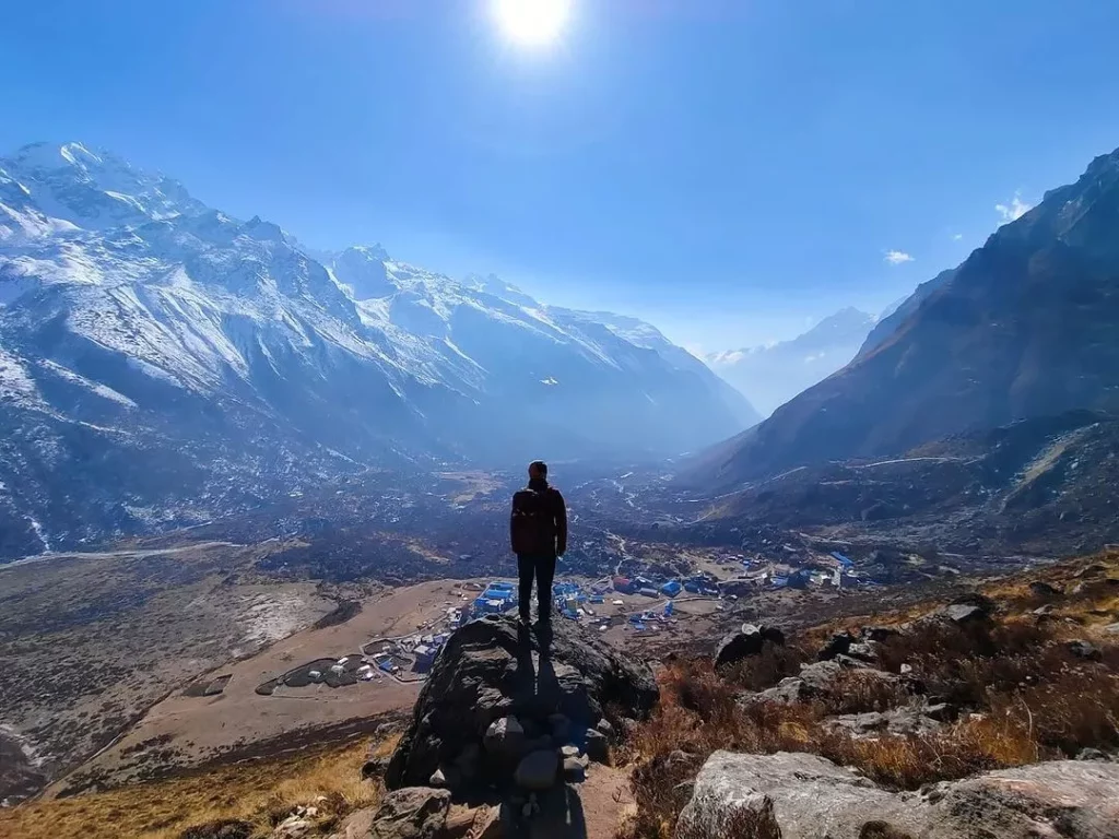 a person standing on a rock looking at a valley with snow covered mountains